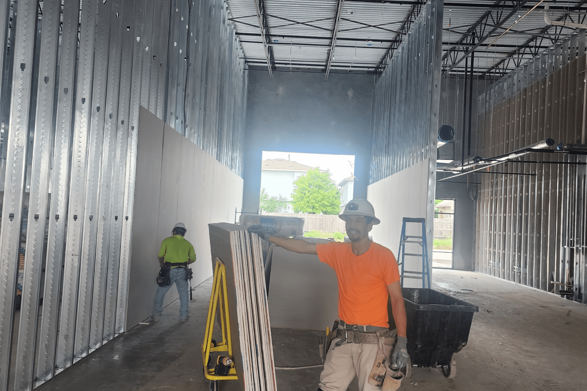 a construction site with a man in an orange shirt standing in the center, holding a hammer